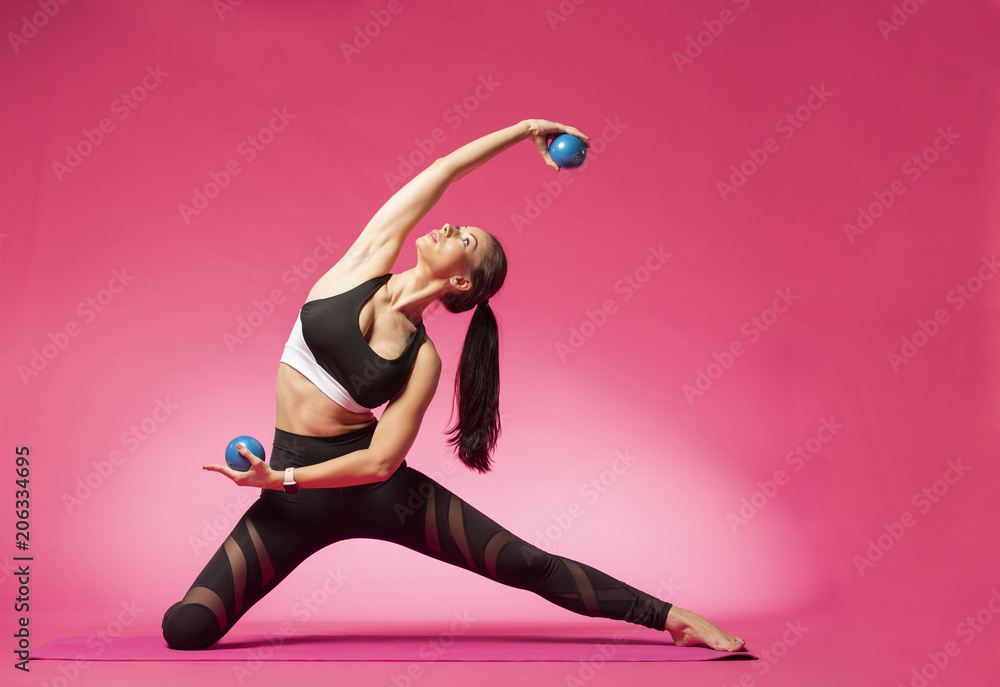 Wall mural long haired beautiful pilates or yoga athlete does a graceful pose with blue exercise balls while we