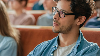 Fototapeta premium Handsome and Smart Hispanic Man Listens to a Lecture in a Classroom Full of Multi Ethnic Students. Shallow Depth of Field.