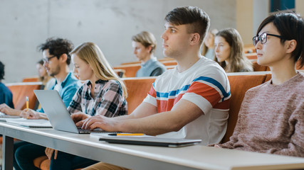 Handsome Caucasian Student Uses Laptop while Listening to a Lecture at the University. Multi Ethnic Group of Modern Bright Students Invested in Their Future.