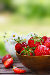 Fresh strawberries in a bowl on wooden table with natural green background, vertical