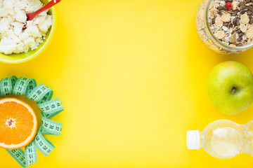 Fruits, curd, measuring tape, water and muesli on the yellow background. Weight loss, diet controlled healthy food concept background. Top view, close up.