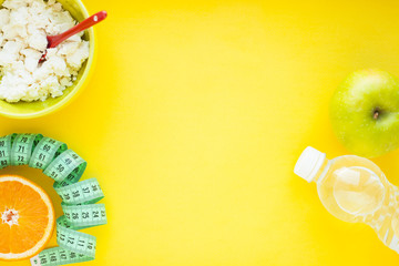 Fruits, curd, measuring tape, water and muesli on the yellow background. Weight loss, diet controlled healthy food concept background. Top view, close up.