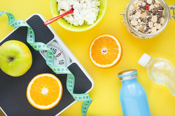 Fruits, curd, measuring tape, water and muesli on the yellow background. Weight loss, diet controlled healthy food concept background. Top view, close up.