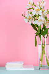 two white books and bouquet of alstroemeria flowers on tabletop on pink