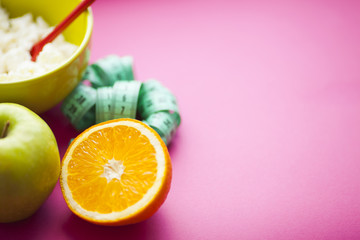 Fruits, curd, measuring tape, water and muesli on the pink background. Weight loss, diet controlled healthy food concept background. Top view, close up.