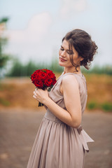 Portrait of a beautiful bridesmaid posing with wedding bouquet outdoor. Woman with flowers at park. Amaizing wedding day.
