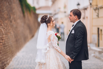 Happy newlywed couple on a walk in old European town street, gorgeous bride in white wedding dress...