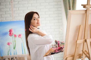 woman paints picture on canvas with oil paints in her studio