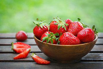 Fresh strawberries in a bowl on wooden table with natural green background