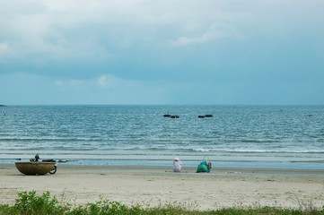 Fototapeta na wymiar A woman sitting on a beach near her traditional fishing boat, overlooking the sea.