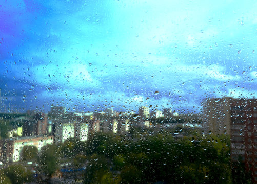 raindrops on the window behind which the big city and blue sky in the clouds are visible