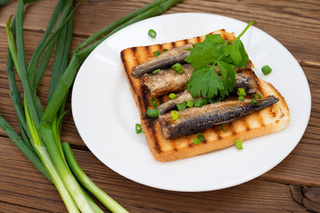 Smoked sprats on toast with parsley and leek on wooden background.