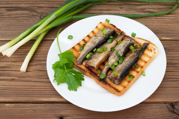 Smoked sprats on toast with parsley and leek on wooden background.
