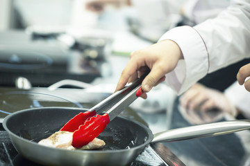 Cook prepares the chicken in a frying pan.