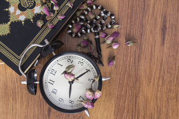 Koran, black clock and rosary on the wooden background with rose for Islamic concept. Holy book Quran for Muslims for eleven month sultan Ramadan.