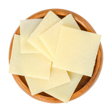 Parmesan cheese slices in wooden bowl. Parmigiano-Reggiano. Italian hard, granular cheese, of slightly yellow color, made of unpasteurized cow milk. Macro food photo, closeup, from above, over white.