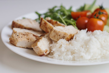 White rice, chiken breast and fresh organic vegetables on white plate. Healthy and balanced meal. Diet food