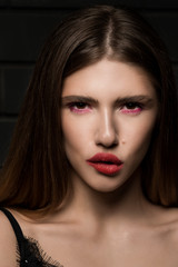 Close-up portrait of a beautiful fashion girl with big red lips on the background of a black brick wall,  in a black sexy singlet. Biting his lip. Look. Bright sexy makeup.