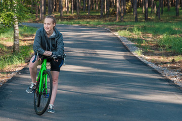 Naklejka premium Girl on a bicycle in a grey hoodie in the park. Races on a bicycle. Active way of life and playing sports.