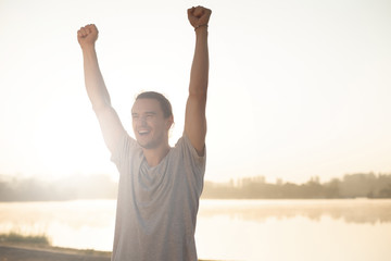 Sweaty man with raised hands happy to finish workout on sunrise