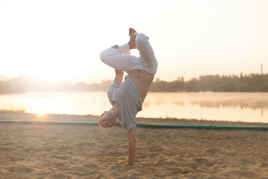Athletic capoeira performer workout training on the beach sunris