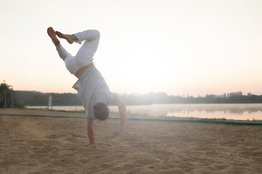 Athletic capoeira performer workout training on the beach sunris