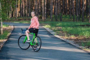 Girl on a bicycle in a pink hoodie in the park. Races on a bicycle. Active way of life and playing sports.