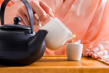 partial view of woman pouring tea into cup while having tea ceremony at home