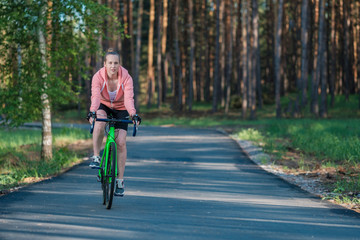 Girl on a bicycle in a pink hoodie in the park. Races on a bicycle. Active way of life and playing sports.