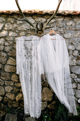 Wedding dress and boudoir of the bride hang on hangers on horns on a stone wall near the house