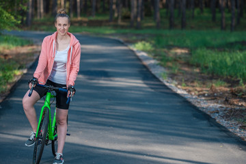 Girl on a bicycle in a pink hoodie in the park. Races on a bicycle. Active way of life and playing sports.