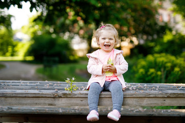 Cute adorable toddler girl playing with blooming chestnut flowers. Little baby child going for a walk on sunny day.