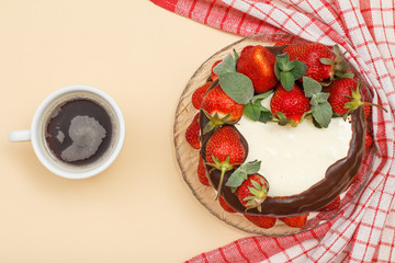 Homemade chocolate cake decorated with fresh strawberries on glass plate with kitchen napkin and cup of coffee