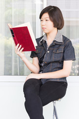Young woman reading book sitting on chair