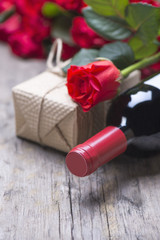 A bottle of red wine, a gift, a bouquet of red roses on a rustic old vintage background
