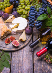 Two bottle of red and white wine, grapes, cheese, cork, corkscrew, white bread on a dark background