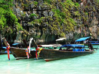 Longtale boats at the Phuket beach with limestone rock on background in Thailand. Phuket island is a most popular tourist destination in Thailand.