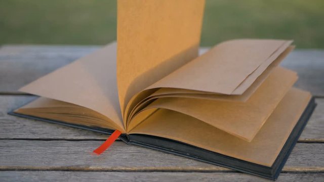 Wind turns the pages of a blank book lying on a bench. Very nice and designer notebook on the street.