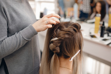 Fototapeta premium Woman hairdresser making hairstyle to blonde girl in beauty salon.