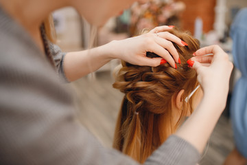 Woman hairdresser making hairstyle to blonde girl in beauty salon.