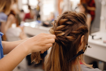 Woman hairdresser making hairstyle to blonde girl in beauty salon.