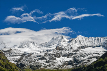 Beautiful view of the snowy peaks of the Italian Alps in Val d'Aosta. Panorama of snow-covered mountains with blue sky and clouds. Summer landscape from Bionaz on the mounts behind the Prarayer refuge