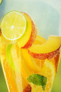 Fruit soda limanade close-up in a glass container, a variety of pieces of summer fruit and gas bubbles.
