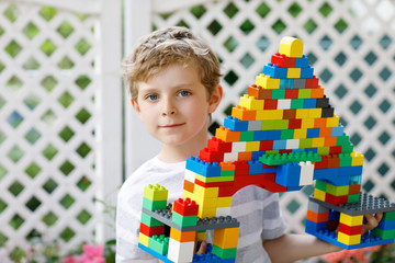 Little blond child and kid boy playing with lots of colorful plastic blocks.