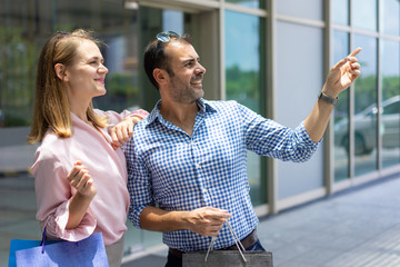 Happy mid adult man with shopping bag pointing direction to wife