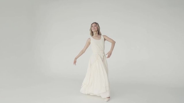 cute young ballerina gracefully dancing in white fluttering dress in white studio. slow motion