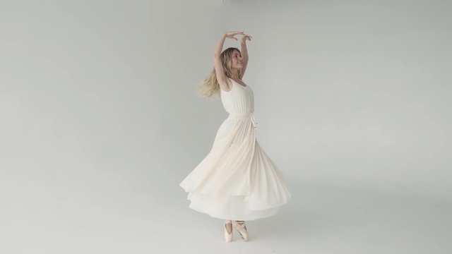 A young ballerina smiles and elegantly dances on tiptoe in a fluttering light dress and pointe. slow motion