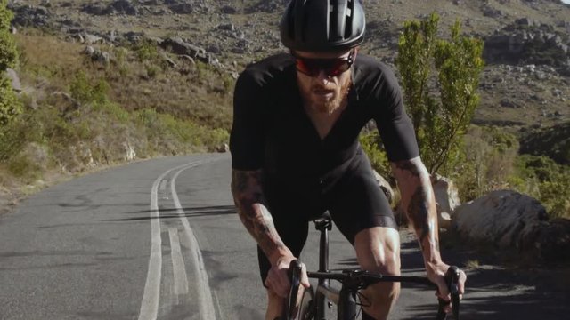 Slow motion video shot of a professional male cyclist doing uphill out of the saddle on road bike. Sportsman climbing up the hill on a bicycle. 
