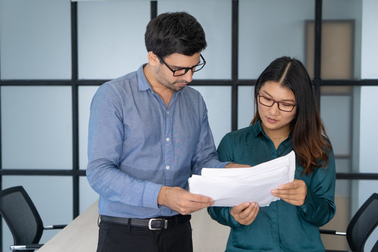 Caucasian boss giving papers to Asian assistance