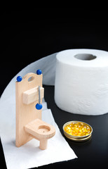 Wooden toy toilet, capsules and paper on black background